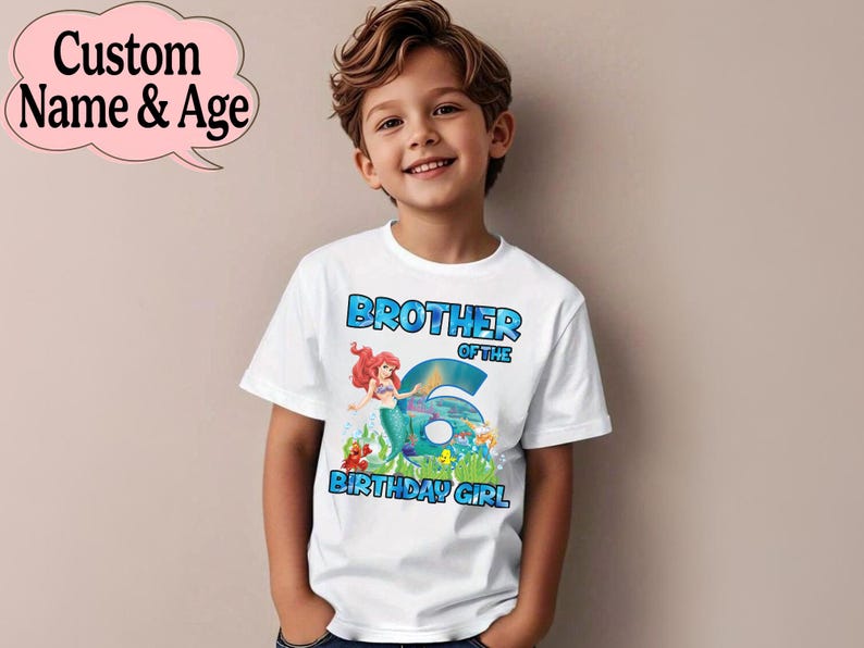May include: White t-shirt with the text "BROTHER OF THE 6 BIRTHDAY GIRL" in blue. The shirt features a mermaid graphic. A pink speech bubble with the text "Custom Name & Age" is in the upper left corner. The shirt is worn by a young boy.
