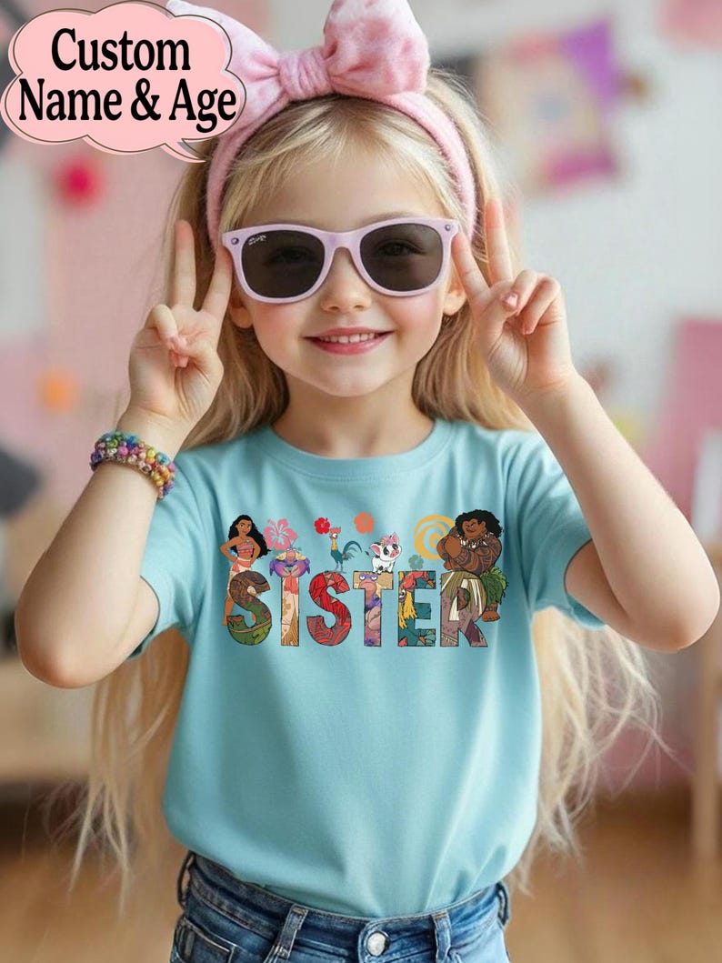 May include: A light blue t-shirt with the word "SISTER" in colorful letters, featuring cartoon characters. The shirt is worn by a young girl wearing pink sunglasses and a matching headband. The image includes the text "Custom Name & Age".