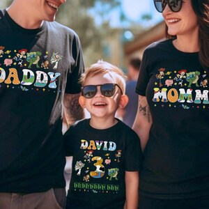 May include: Black t-shirts with colorful graphics featuring characters and text from a popular animated movie. The shirts say "DADDY", "MOMMY", and "DAVID 3rd Birthday Day". The family is wearing sunglasses.
