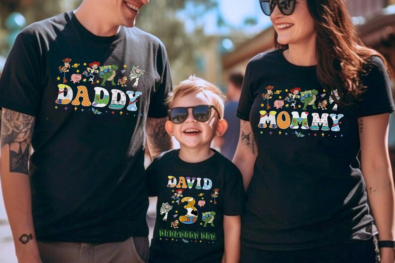 May include: Black t-shirts with colorful graphics featuring characters and text from a popular animated movie. The shirts say "DADDY", "MOMMY", and "DAVID 3rd Birthday Day". The family is wearing sunglasses.