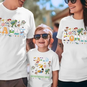 May include: White t-shirts with colorful Toy Story character designs. The shirts feature the words "DADDY", "MOMMY", and "DAVID" in playful fonts, with additional text "Happy Birthday Day". A family wears matching shirts.