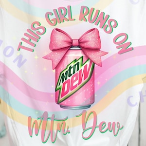 May include: White t-shirt with a graphic of a pink Mtn Dew can adorned with a pink bow. The text "THIS GIRL RUNS ON" arches above the can, and "Mtn. Dew" is written below in green script.