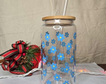 May include: A clear glass reusable water bottle with a bamboo lid and a blue and yellow floral pattern. The bottle has a clear plastic straw inside.