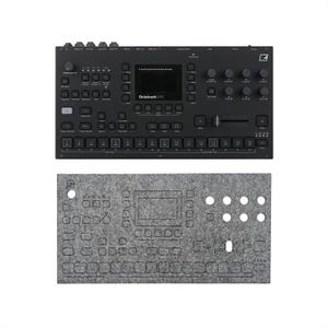 May include: Black electronic music production device with numerous buttons, knobs, and a screen, labeled "Octatrack MKII." Below it is a gray felt cover with cutouts for the device's controls. The device is designed for live performance and studio use.