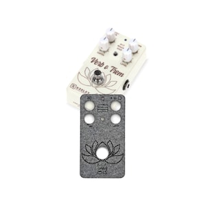 May include: A white Keeley Electronics Verb o Trem guitar effects pedal with four knobs labeled "Depth", "B+T Mix", "Rate", and "Level". The pedal has a brown lotus flower design and the text "Verb o Trem" printed on the front. A gray felt pedalboard patch with a black lotus flower design is also shown.