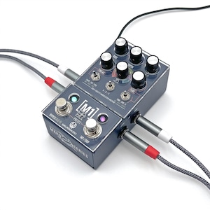 May include: Two dark gray guitar effect pedals with multiple knobs, switches, and input jacks. The pedals are connected with gray and red cables. The text "M1" and "MAKOS SERIES" are visible on the pedals.