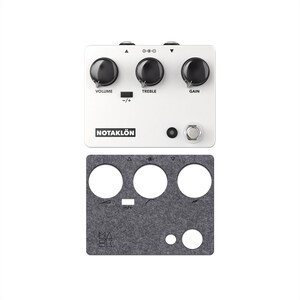 Puede incluir: Un pedal de efectos para guitarra blanco con la etiqueta NOTAKLÖN, tres perillas negras para volumen, agudos y ganancia, un interruptor pequeño y un pedal metálico. Debajo hay una cubierta de fieltro gris oscuro con recortes para los controles.