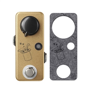 May include: A gold-colored guitar effects pedal featuring a large black control knob, a silver footswitch, and a graphic of rabbit ears emerging from a top hat. Beside it is a grey felt overlay with matching cutouts and the text MASK.