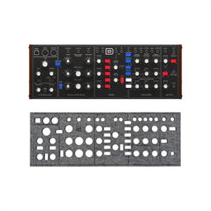 May include: A black synthesizer with numerous knobs, buttons, and sliders, featuring red, white, and blue accents. The synthesizer has a dark wood-grain frame. Below it is a grey felt panel with various cut-out shapes.