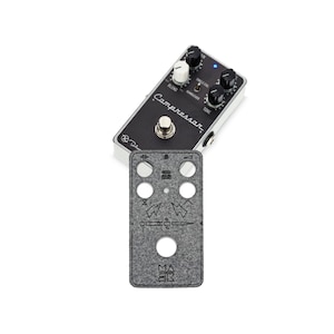 Pode incluir: Um pedal de efeitos para guitarra preto e prateado com a etiqueta "Compressor", com vários botões e um interruptor de pé. Uma capa de feltro cinza com orifícios recortados e símbolos gravados está abaixo do pedal.