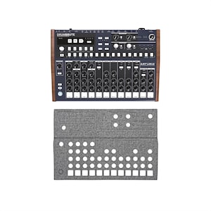 Op de afbeelding: Een zwarte en zilveren Arturia DrumBrute impact drumcomputer met houten zijpanelen. Het apparaat heeft tal van knoppen, knoppen en een beeldscherm. Daaronder bevindt zich een grijze schuimrubberen inzet met uitsparingen voor de machine.