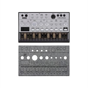 May include: A silver and black Korg Volca Bass synthesizer with numerous knobs, buttons, and a digital display. Below it is a gray felt cover with cutouts for the controls. The text "KORG" and "Volca Bass" are visible.