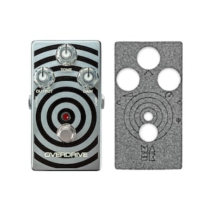Puede incluir: Un pedal de overdrive de guitarra plateado y negro con un diseño circular y tres perillas etiquetadas como "Tone", "Gain" y "Output". El pedal tiene una luz LED roja y un interruptor de pie negro etiquetado como "Overdrive".