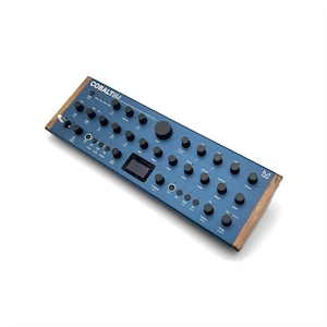 Può includere: Un sintetizzatore blu con numerosi pulsanti neri e un piccolo schermo. Il testo "COBALT8M" è stampato in alto a sinistra. I lati sono rifiniti in legno. Un moderno strumento musicale elettronico.
