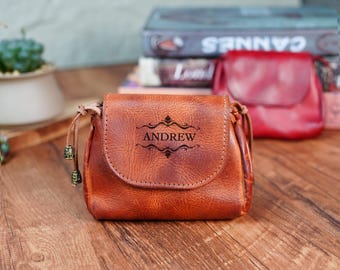 May include: A brown leather purse with a flap closure and a decorative strap. The purse is personalized with the name "ANDREW" in a decorative font.