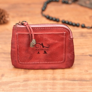 May include: A red leather zippered pouch with a personalized monogram of the letter "A" and the name "ANTHONY" engraved on the front.