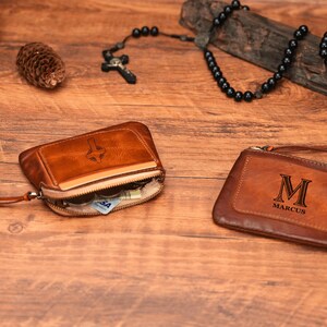 May include: Two brown leather wallets with zipper closures. One wallet has a cross design and the other has the letter "M" and the name "Marcus" engraved on it.