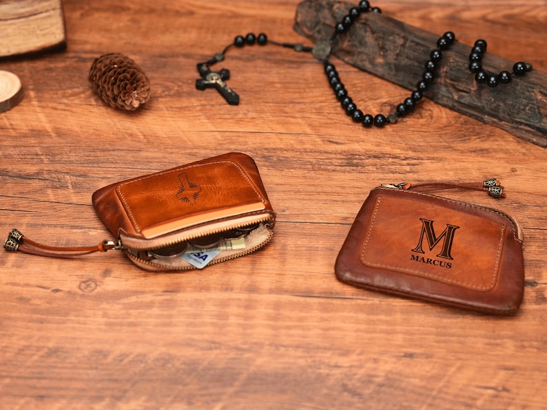 May include: Two brown leather wallets with zipper closures. One wallet has a cross design and the other has the letter "M" and the name "Marcus" engraved on it.