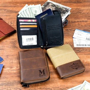 Könnte beinhalten: Eine Auswahl an Reißverschluss-Geldbörsen in verschiedenen Designs. Eine schwarze Geldbörse ist geöffnet und zeigt Kreditkartenfächer, Bargeld und einen Reisepass. Eine braune Ledergeldbörse ist mit dem Buchstaben "M" und dem Namen "Marcus" geprägt.