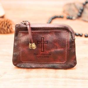 May include: A brown leather zippered pouch with a cross and the text "First Communion April 1, 2025" engraved on the front.