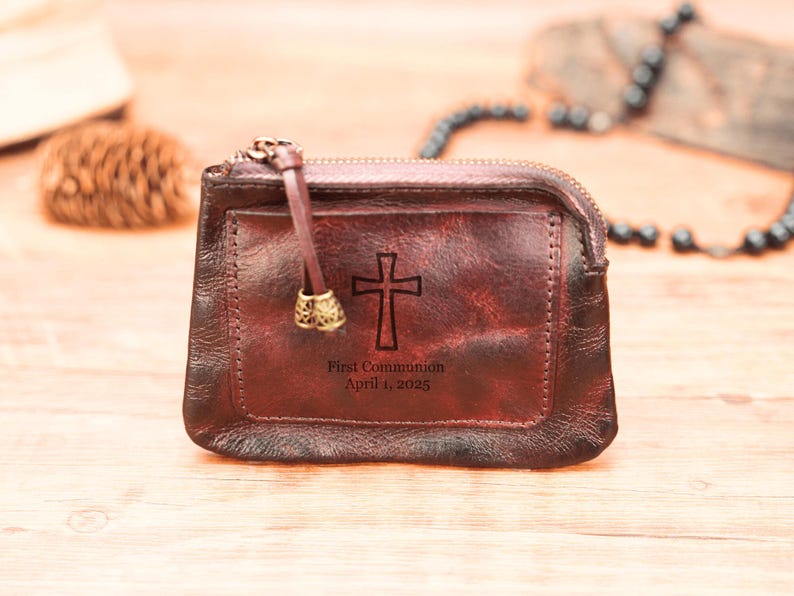 May include: A brown leather zippered pouch with a cross and the text "First Communion April 1, 2025" engraved on the front.