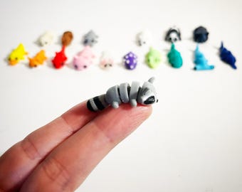 May include: A small, gray and black raccoon figurine curled up in a sleeping position. The figurine is made of polymer clay and is about 2 inches long.