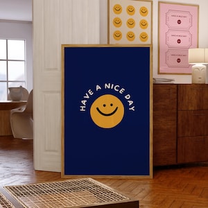 Op de afbeelding: Een ingelijste marineblauwe poster met de tekst 'HAVE A NICE DAY' en een gele smiley. Andere ingelijste posters met smileys en ticketontwerpen zijn zichtbaar op de achtergrond. De frames hebben een natuurlijke houten afwerking.