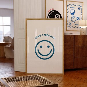 May include: A framed print with a large blue smiley face and the text "HAVE A NICE DAY". Two other framed prints are visible, one with a pool ball and the text "LUCKY YOU", and another with a wine glass and the text "MORE WINE".