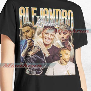 May include: A black t-shirt with a vintage-style graphic featuring multiple men with the text "Alejandro Rauw" in gold lettering.