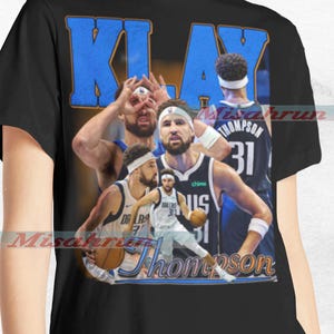 May include: A black t-shirt featuring a collage of basketball player Klay Thompson in various poses. The shirt displays the text "Klay Thompson" in a blue and orange font.