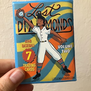 Può includere: Una confezione rettangolare di figurine Lost Diamonds Volume Two AFAB Baseball con un'illustrazione di un giocatore di baseball in divisa bianca che afferra un diamante. Lo sfondo presenta strisce diagonali arancioni e gialle.