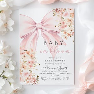 Könnte beinhalten: Eine rosafarbene Babyparty-Einladung mit einer großen rosafarbenen Schleife und Aquarellblumen. Der Text lautet "Baby in Bloom" und enthält den Namen "Olivia Smith" sowie Details zur Party.