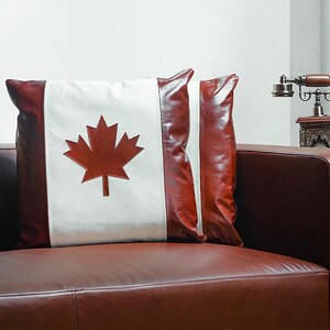 May include: Two decorative throw pillows with a Canadian flag design. One pillow features a red maple leaf on a white background with red leather borders. The other pillow is solid red leather.