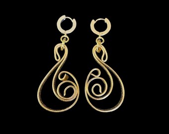 May include: A pair of gold-toned dangle earrings with a swirling, abstract design. The earrings are made of wire and have a hoop closure.