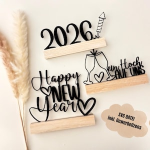 Puede incluir: Recortes de madera negros para Año Nuevo y celebraciones. Los recortes incluyen el año "2026" con un fuegos artificiales, "Happy New Year" con un corazón, y un diseño con dos copas de champán y el texto "ein Hoch auf uns".