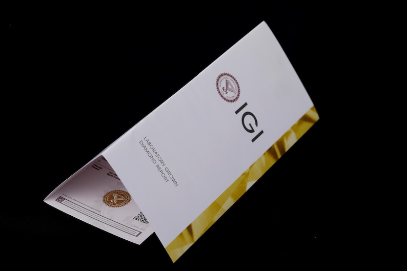 Może przedstawiać: Raport IGI dotyczący hodowanych w laboratorium diament&oacute;w, w kolorze białym i złotym. Raport zawiera logo IGI i słowa "Laboratory Grown Diamond Report".