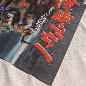 May include: A poster featuring artwork from "Howl's Moving Castle." The image shows a detailed illustration of a mechanical structure with smoke, set against a landscape. Japanese text is prominently displayed in red.
