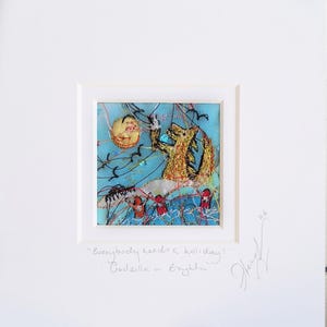 May include: A framed textile art piece featuring a yellow creature on a light blue background with a sun, birds, and red figures. The text below reads: "Everybody needs a holiday!" "Godzilla in Brighton". A signature and the number 26 are visible.