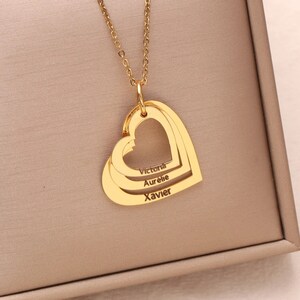May include: Gold necklace with three interlocking heart charms. The hearts are engraved with the names "Victoria", "Aurelie", and "Xavier".
