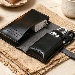 May include: A black leather tech organiser case featuring a flap with the engraved text Merry Christmas, may you always be safe and happy and a pocket with the name Christie engraved on it, containing a white power adapter and two USB cables.