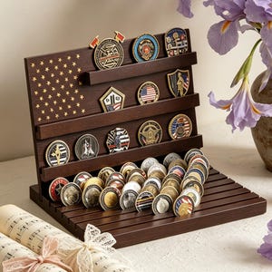 May include: A dark brown wooden display stand featuring a carved American flag pattern on the back panel. The stand has multiple horizontal shelves and grooves designed to hold and showcase a collection of various circular and shaped challenge coins.