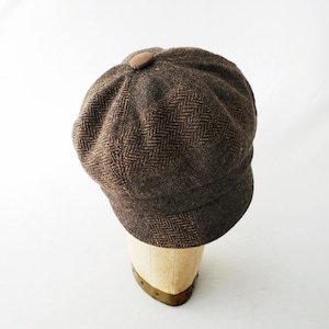 May include: A brown tweed newsboy cap with a button on top. The cap is on a mannequin head.