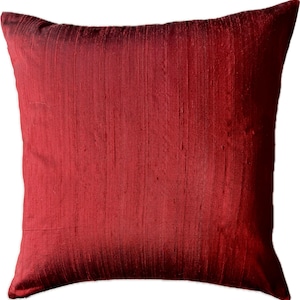 Pode incluir: Uma almofada de cor vermelha escura com uma textura suave e sedosa. A almofada é feita de um tecido luxuoso e tem um brilho sutil.