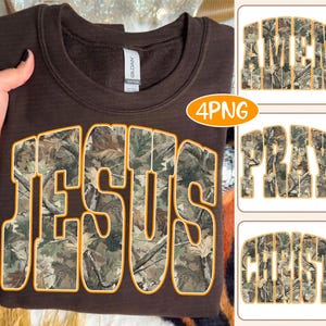 May include: A brown sweatshirt with the word "JESUS" in large, bold letters across the front. The letters are filled with a camouflage pattern and outlined in orange. Additional graphics with the words "AMEN", "PRAY", and "CHRIST" are also visible.