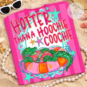 May include: A pink t-shirt with the text "HOTTER THANA HOOCHIE COOCHIE" in bright colors. The shirt features a cartoon alligator in a pink and orange inner tube. The design includes stars and a wavy border.