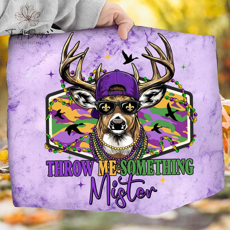 May include: A purple and green graphic featuring a deer wearing a purple cap, sunglasses, and Mardi Gras beads. The deer is set against a camouflage background with the text "THROW ME SOMETHING Mister".