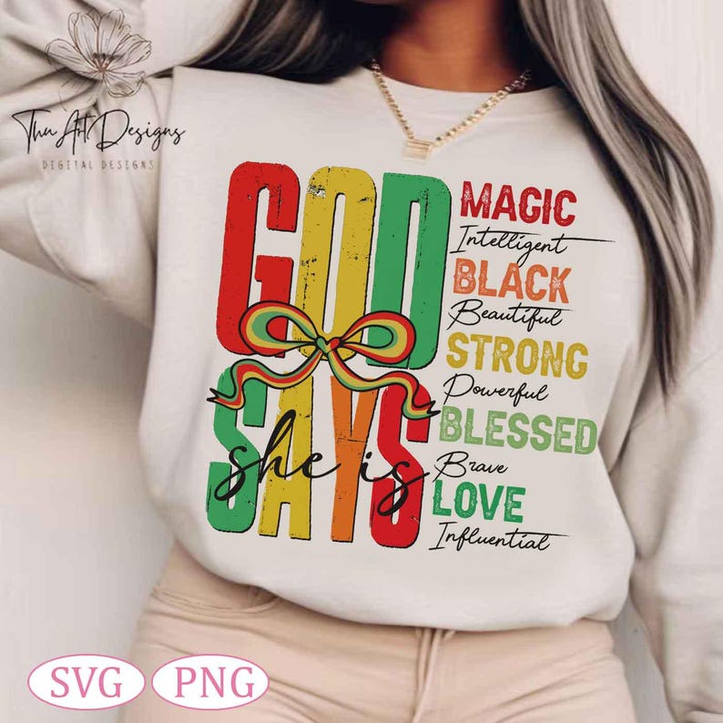 Op de afbeelding: Een wit sweatshirt met een kleurrijk grafisch ontwerp dat "God Says She Is" zegt met de woorden "Magic, Intelligent, Black, Beautiful, Strong, Powerful, Blessed, Brave, Love, Influential" in zwarte tekst.