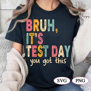 May include: A black t-shirt with a retro-style graphic that says "Bruh, It's Test Day You Got This". The text is in colourful, distressed lettering.