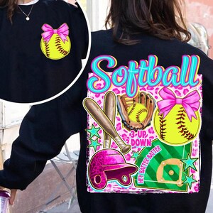 May include: Black sweatshirt with a softball theme. The design includes a yellow softball with a pink bow, a pink helmet, bats, a glove, and the word "Softball" in turquoise. The background has a pink leopard print.
