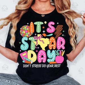May include: Black t-shirt with a colorful graphic that says "It's Star Day" with a Texas outline and other school-themed icons. The text at the bottom says "Don't stress do your best."